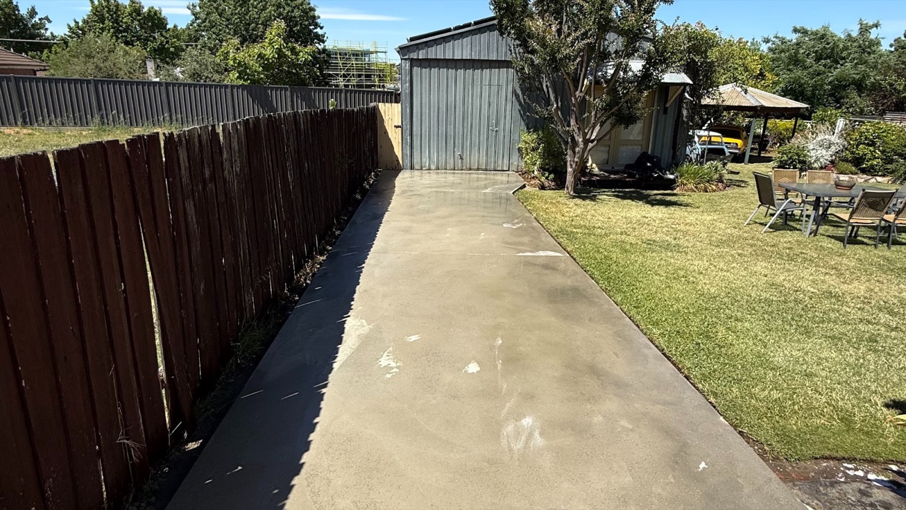 A long concrete path running between a paling fence and a shed to a back yard