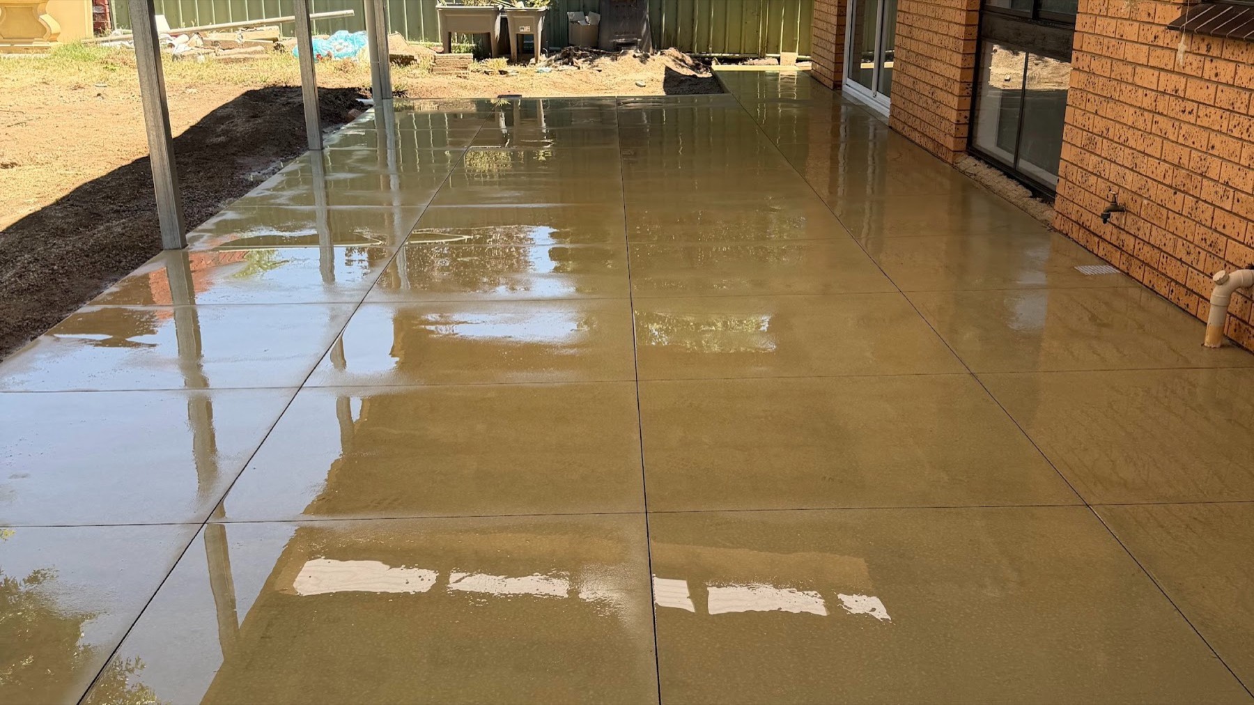 A freshly poured concrete slab running under a verandah beside a brick wall