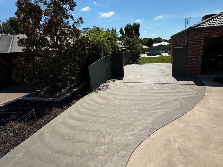 A curved plain concrete driveway sweeping up to a home under gum trees