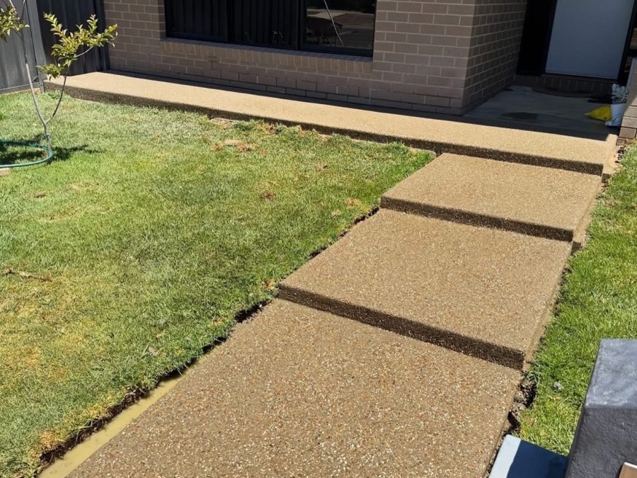 An exposed aggregate path running beside a lawn to a brick house