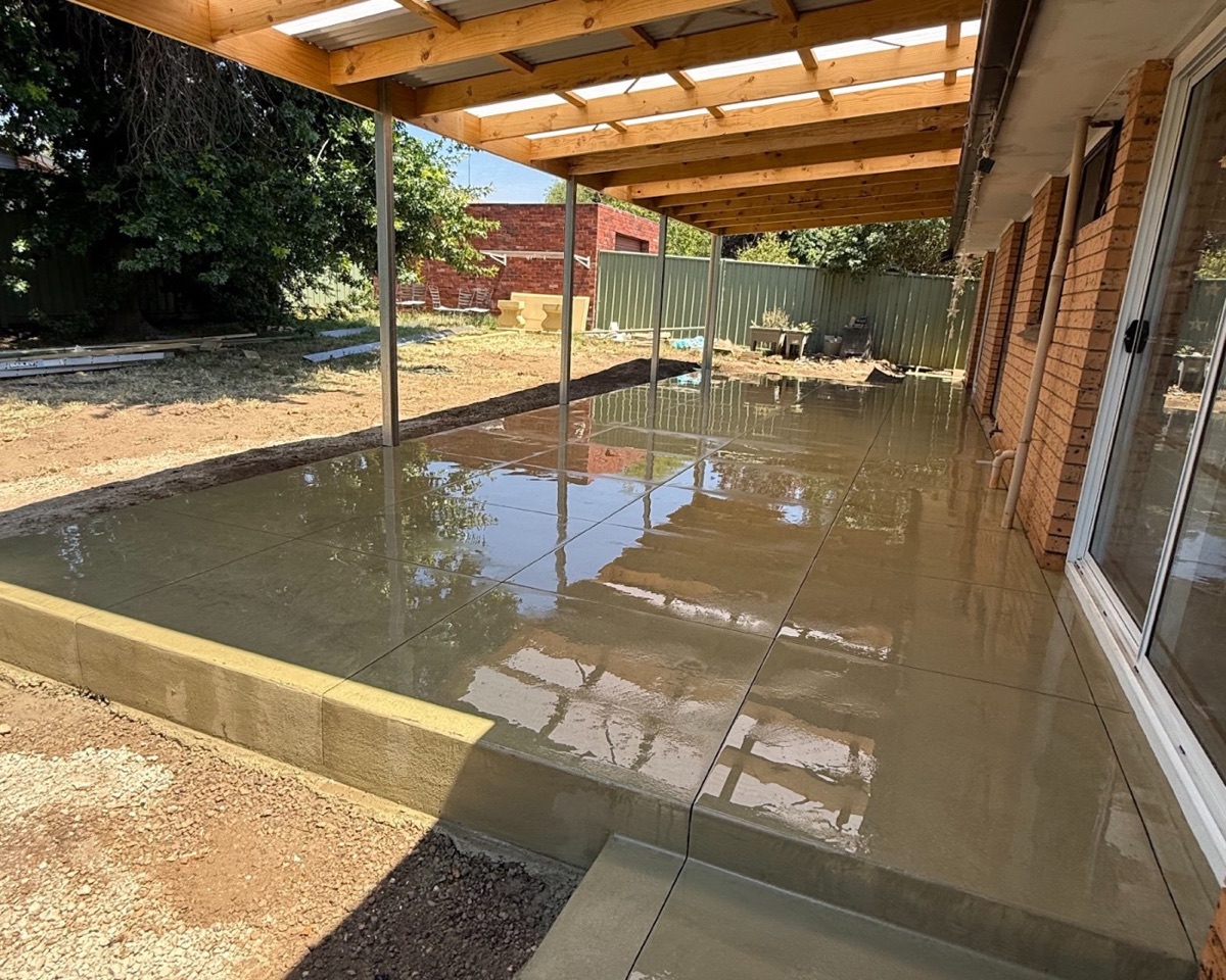 A freshly poured alfresco slab under a verandah roof beside a brick home