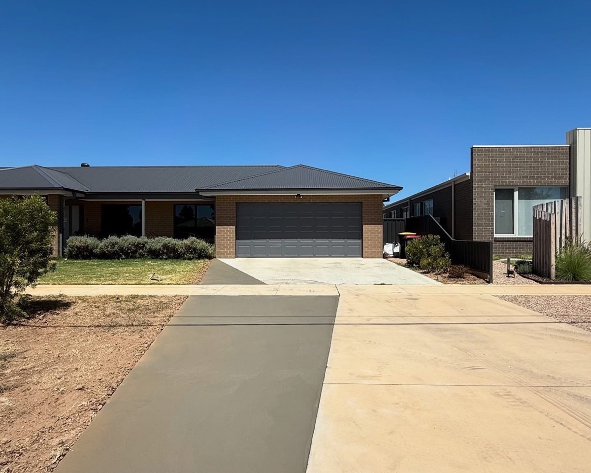 A wide plain concrete driveway running from the street to a double garage
