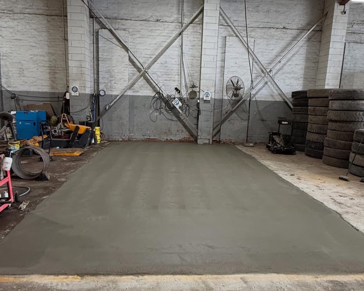 A large plain concrete floor poured inside a shed with steel framing overhead