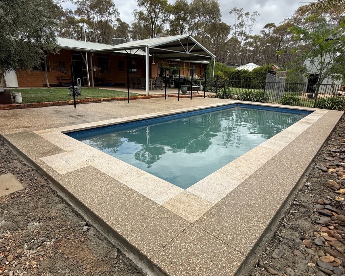 An exposed aggregate pool surround wrapping around a swimming pool with gums behind