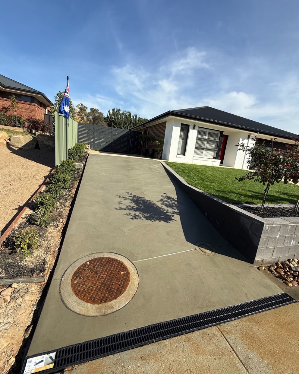 A curved concrete driveway with a formed edge running past a garden bed to a house