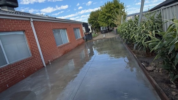 A long concrete path with a wet finish running the length of a red brick wall