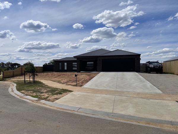 A wide concrete driveway running from the street up to a dark brick home