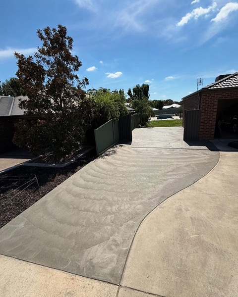 A curved concrete driveway sweeping up to a house under a gum tree