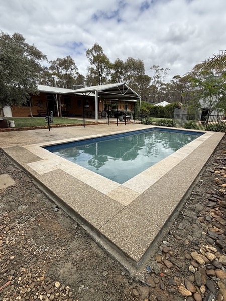 An exposed aggregate pool surround wrapping around a swimming pool