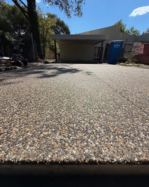 An exposed aggregate driveway running under gum trees toward a carport