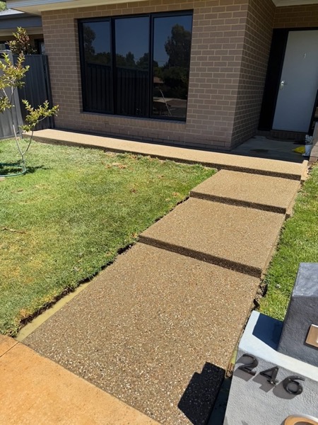 An exposed aggregate path running beside a lawn to a brick house