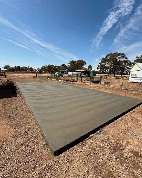 A broad concrete slab poured across a block with gums along the fence