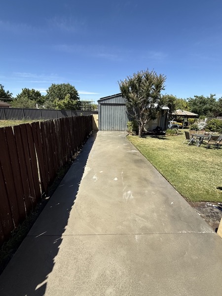 A long concrete path running between a paling fence and a shed