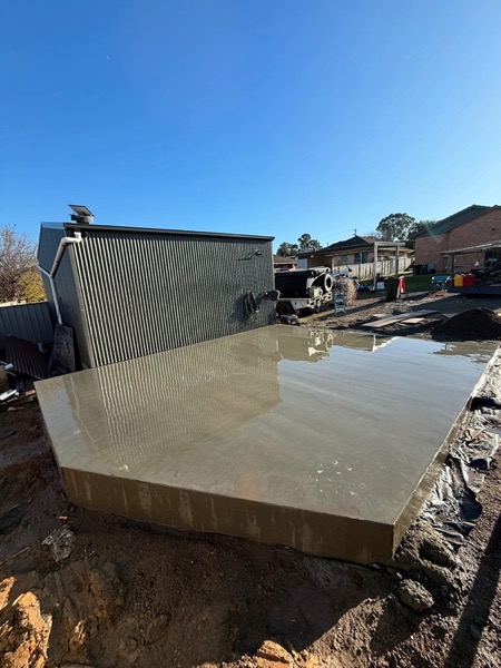 A wide concrete slab poured up against a corrugated shed wall