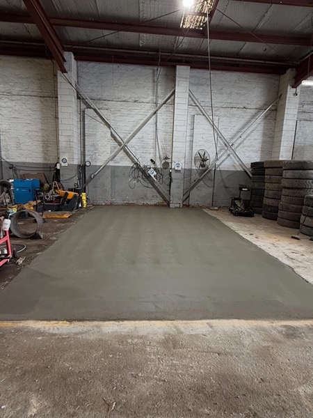 A large plain concrete floor poured inside a shed with steel framing