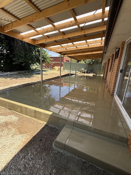 A freshly poured alfresco slab under a verandah roof beside a home