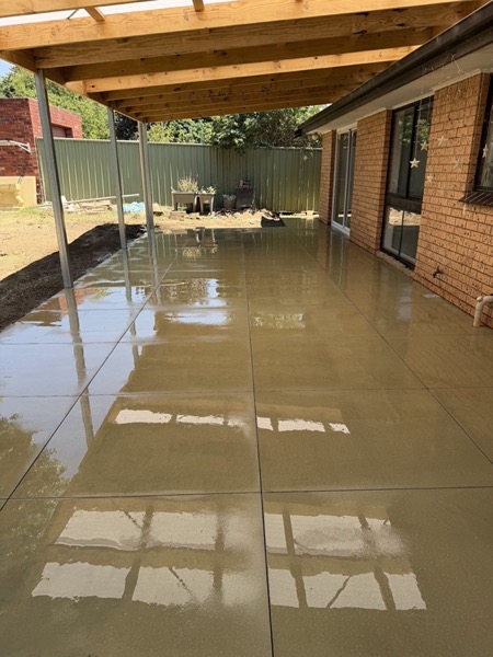 A wet concrete slab poured under a verandah next to a brick wall