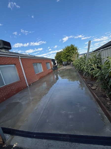 A long concrete path with a wet finish running beside a red brick wall