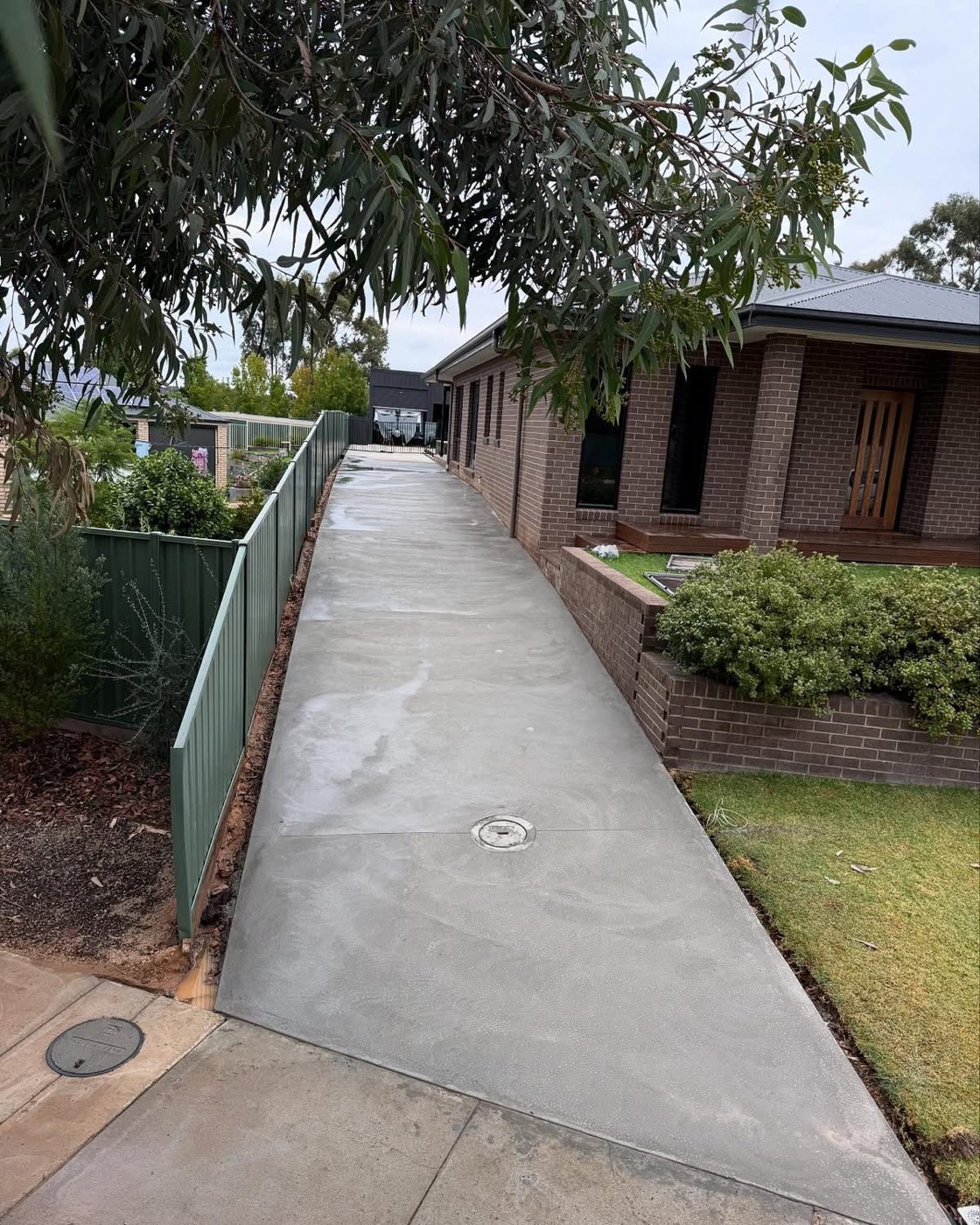 A concrete path running the length of a brick house beside a fence