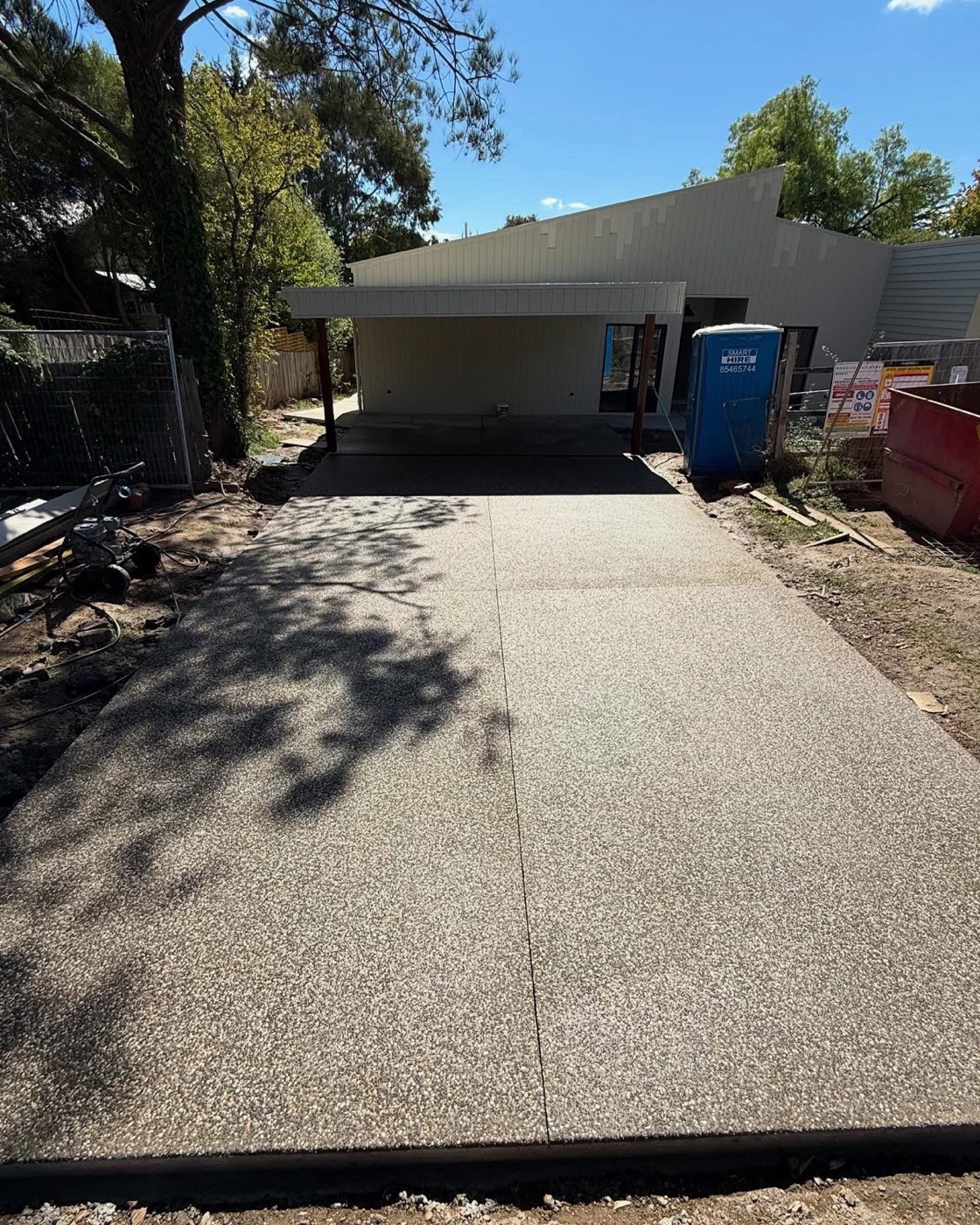 An exposed aggregate driveway running under gum trees to a carport